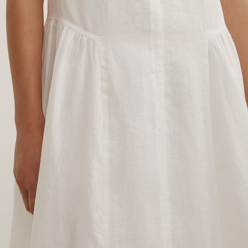 Close-up of a white sleeveless dress with a gathered waist seam, shown on a model against a plain light background.
