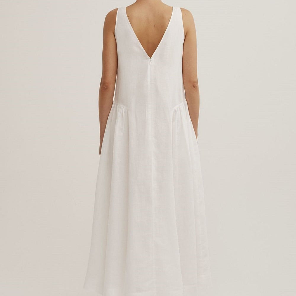 A sleeveless white maxi dress with a deep V-neckline, shown from the back on a model against a plain light gray studio background.